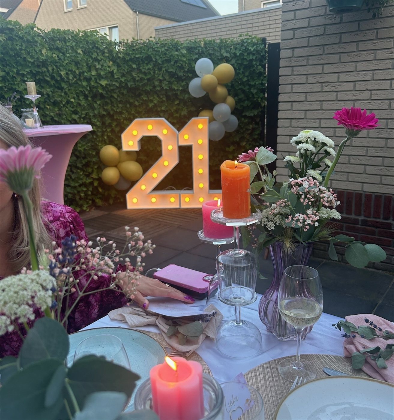 Lichtcijfer 21 met ballonnenboog bij een gedekte feesttafel