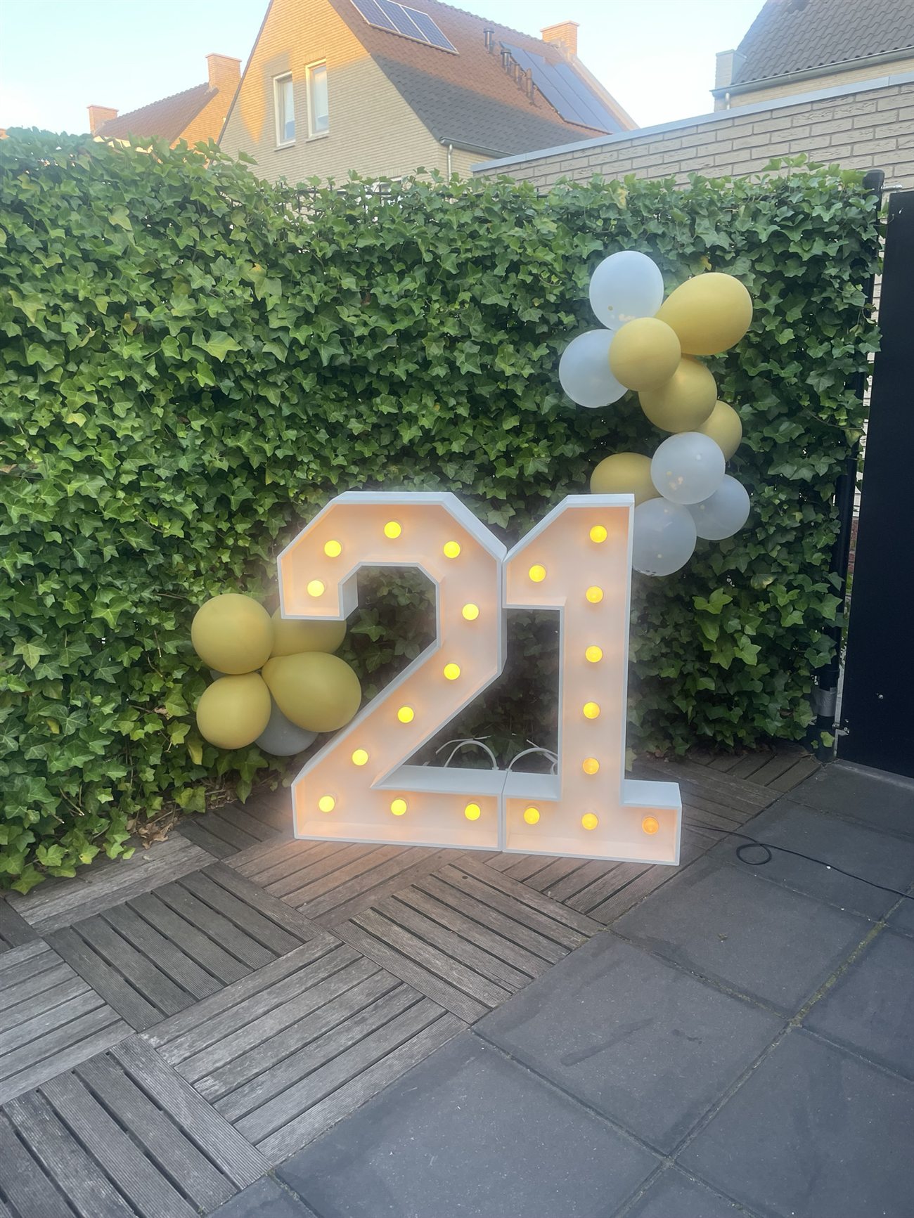 Lichtcijfer 21 met een gouden ballonnenboog bij avond